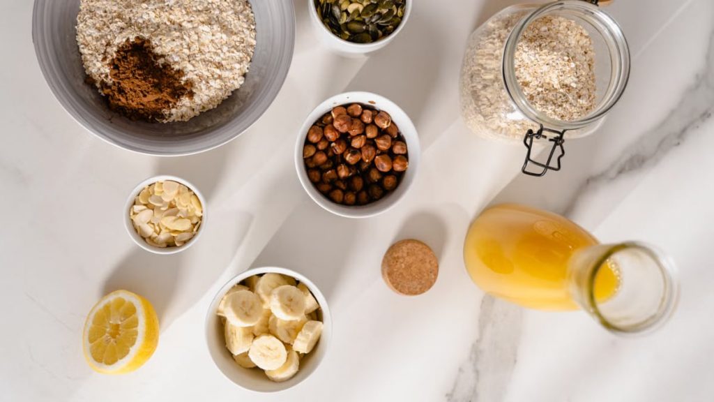 Top view of nutritious breakfast ingredients like oatmeal, nuts, and citrus on a marble surface.