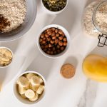 Top view of nutritious breakfast ingredients like oatmeal, nuts, and citrus on a marble surface.