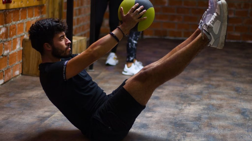 Focused man performing core exercises with a medicine ball in an indoor gym highlighting fitness and strength.